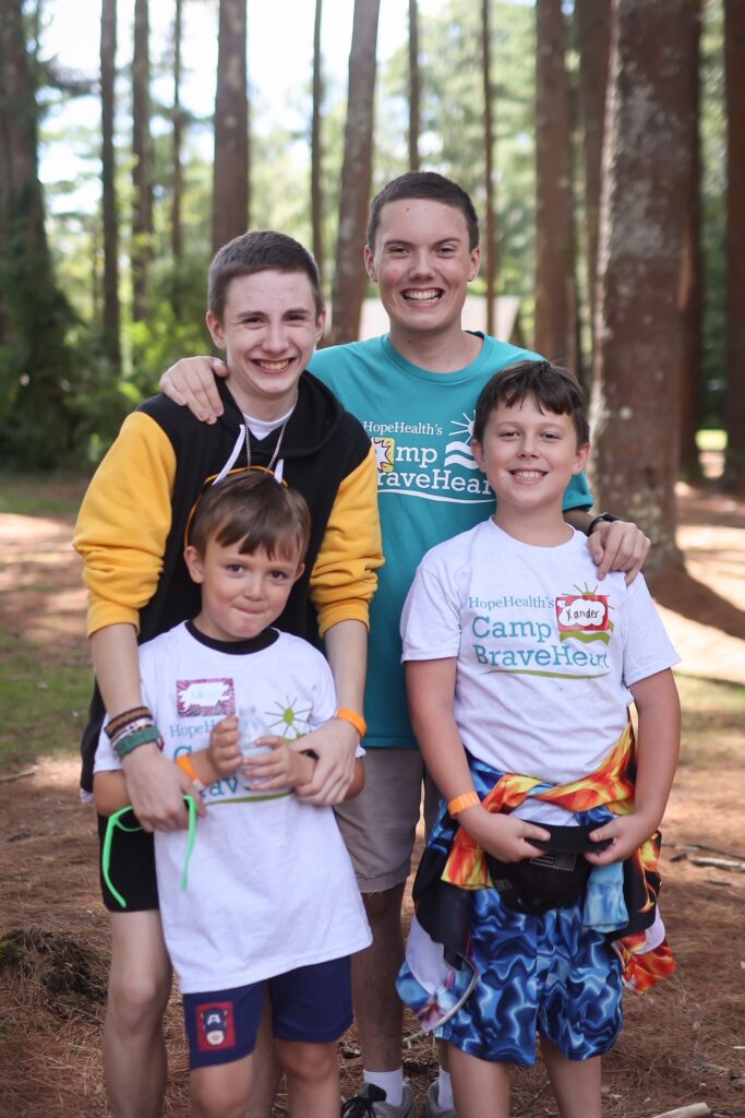 Four boys of varrying ages post in front of a forest of tall trees