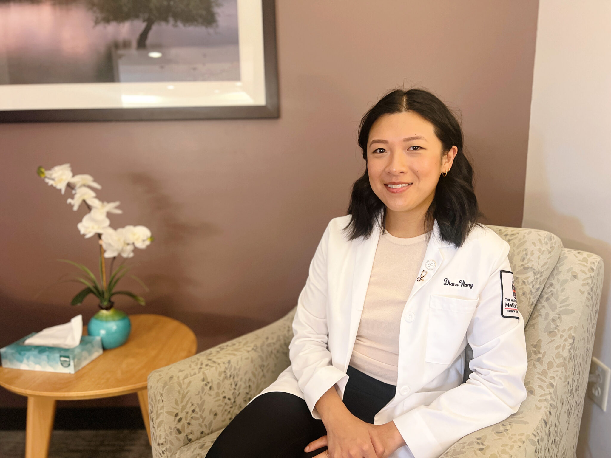 Brown University medical student sitting in chair next to a table with a plant and tissues