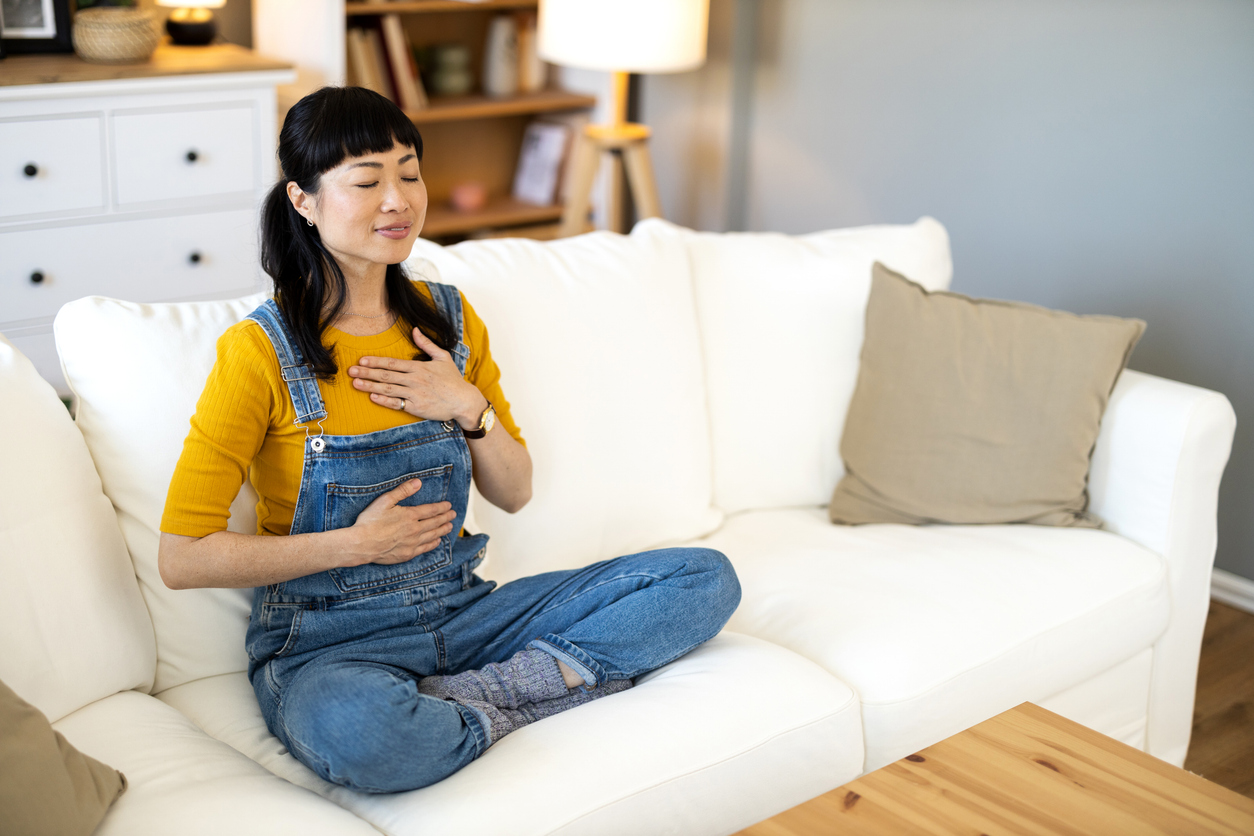 Shot of happy mid adult Asian woman practicing meditation in the living room at home.