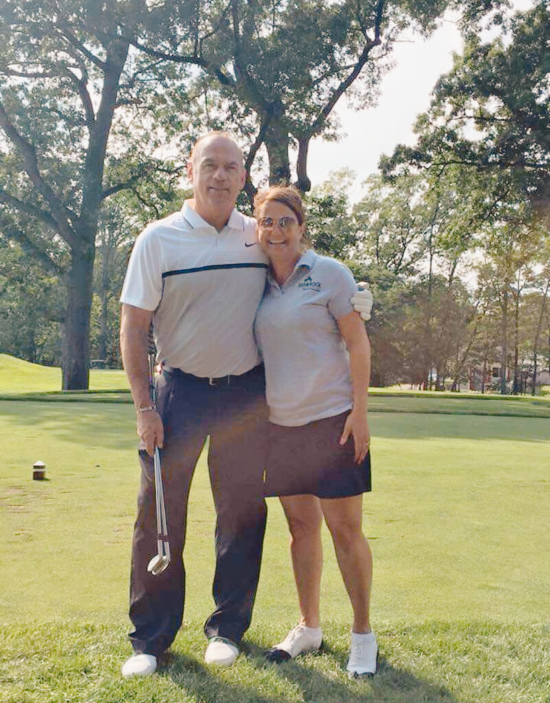 Man and woman standing close together at a golf course, the man is holding a golf club