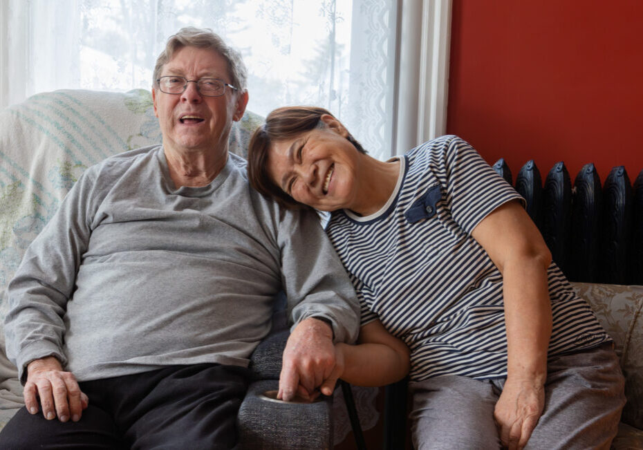 A woman affectionately rests her head on her husbands shoulder, both are warmly smiling at the camera