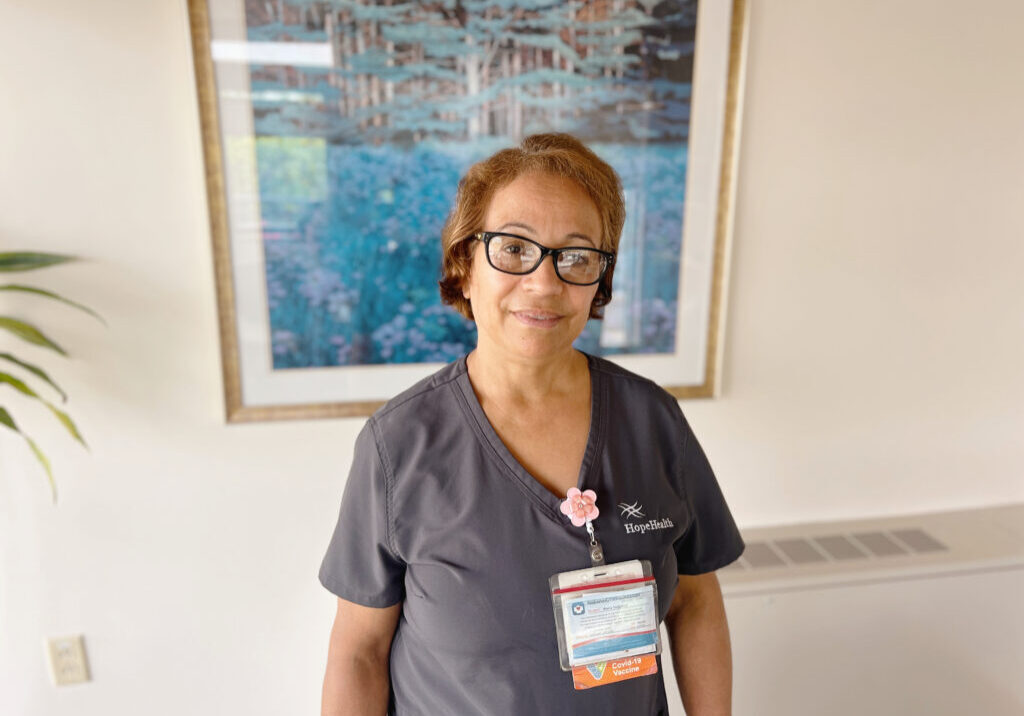 CNA in gray scrubs smiles warmly with compassion in the Hulitar Hospice Center